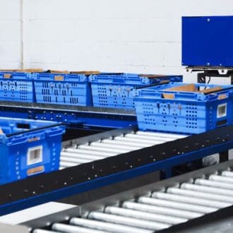 Home 6 Blue grocery totes moving along a conveyor system within the Storix modular staging layout.