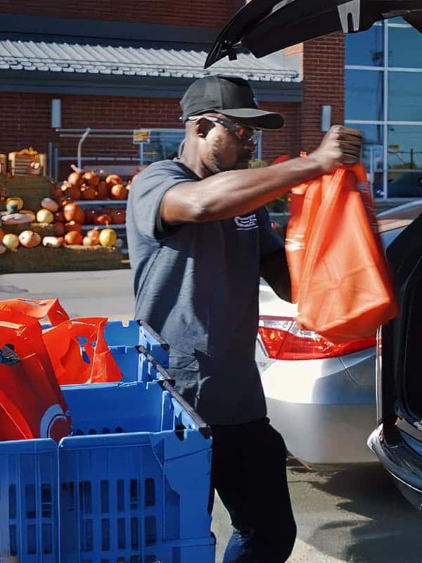800x1080 Associé d’épicerie chargeant les commandes dans un véhicule à l’aide des bacs bleus Storix.